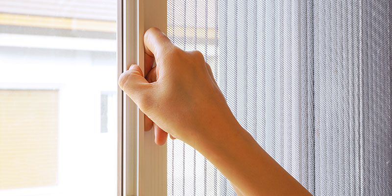Retractable insect screen is fixed on the window and a woman is trying open it.