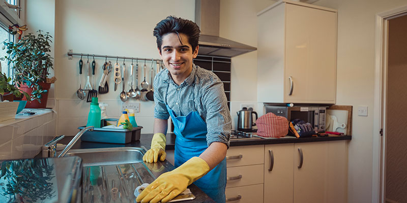 Picture of a teenage boy smiling while cleaning the kitchen