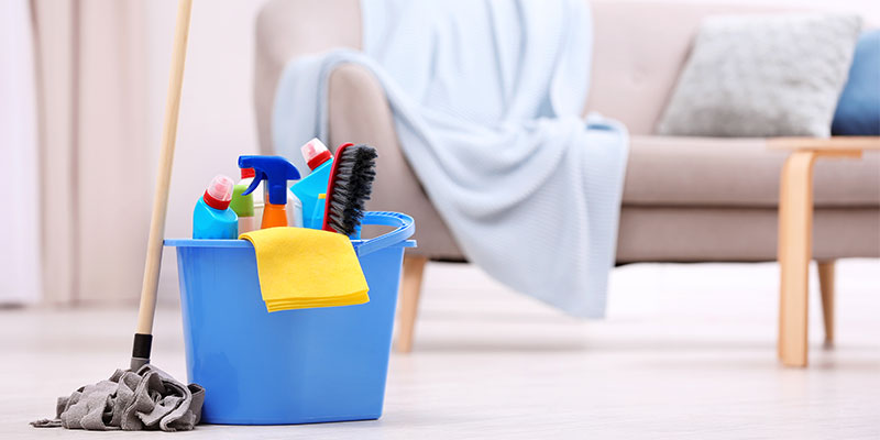 A bucket loaded with cleaning supplies with a mop nearby illustrates the cleaning checklist for a home.