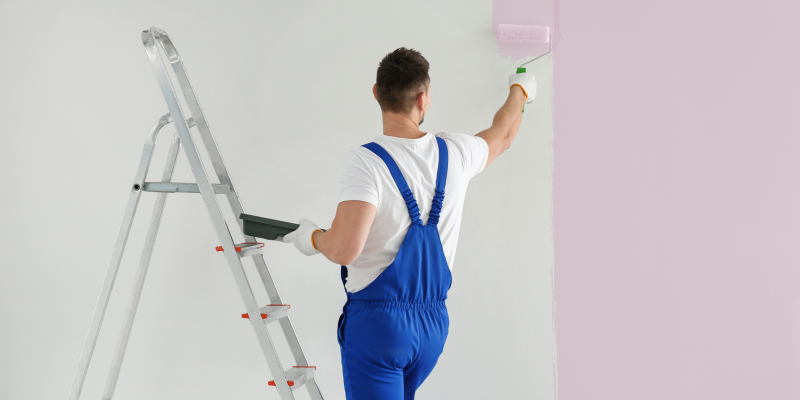 Back view of a professional painter painting wall with light pink dye indoors illustrates the modern painting techniques in home painting.