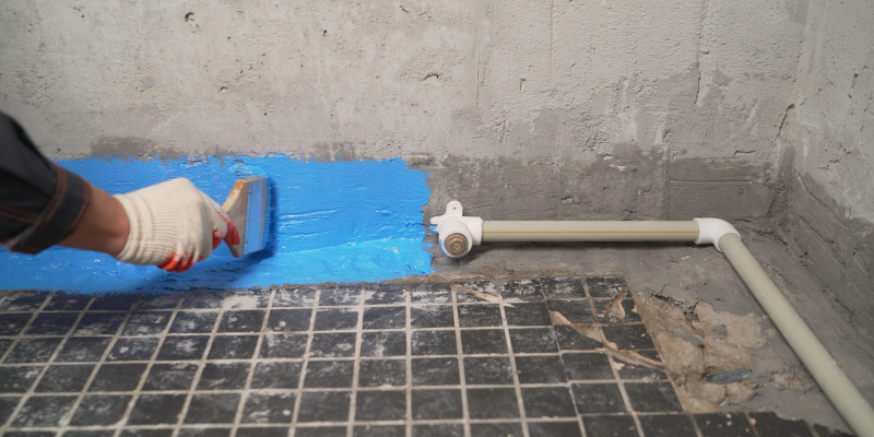 A professional worker paints waterproofing paint on a bathroom floor.