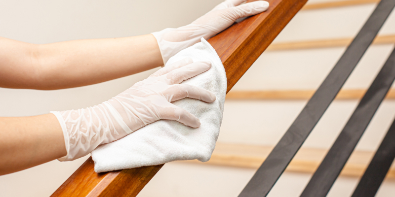 A woman is deep cleaning the stair handle with a cloth.