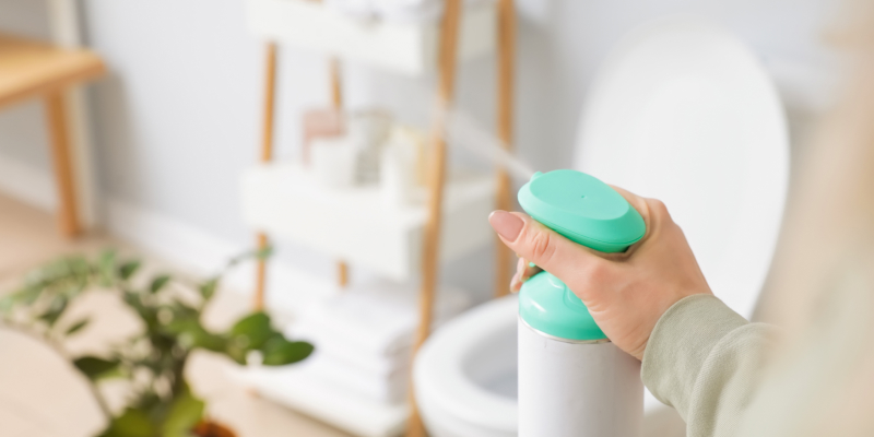 A person using a cleaning spray to address the common causes of bathroom odours for a fresh home.